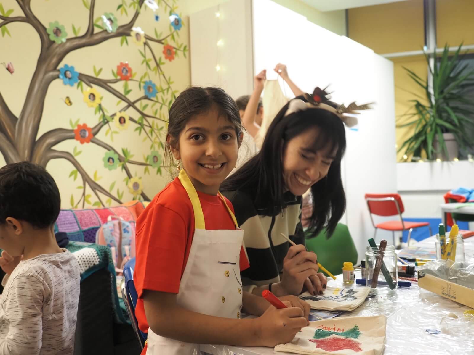 Ein Mädchen und eine ehrenamtliche Mitarbeiterin bemalen Stoffsackerl