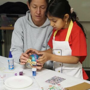 Eine ehrenamtliche Mitarbeiterin verziert mit einem Mädchen Weihnachtskugeln.