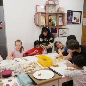 Die Kinder sitzen rund um einen großen Tisch und verzieren Weihnachtskekse.