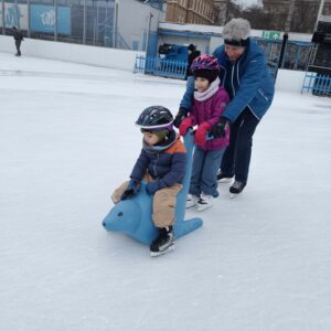 Zwei Kinder werden von einem ehrenamtlichen Mitarbeiter übers Eis geführt