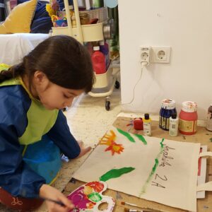 Mädchen bemalt mit bunten Farben eine Tasche