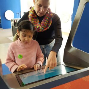 Ein Mädchen und eine Begleitperson bedienen einen Touchscreen