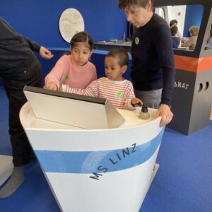 Zwei Kinder und eine Mitarbeiterin des Kinderhospiz Netz vor einem Touchscreen