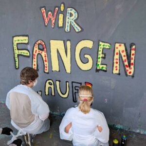 Teenies mit Schutzkleidung und Maske beim Sprayen eines Graffitis.