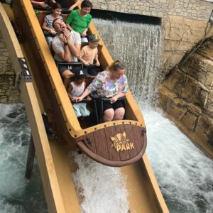 Kinder und erwachsene Begleiter fahren im Familypark mit einem Boot einen Wasserfall hinunter.